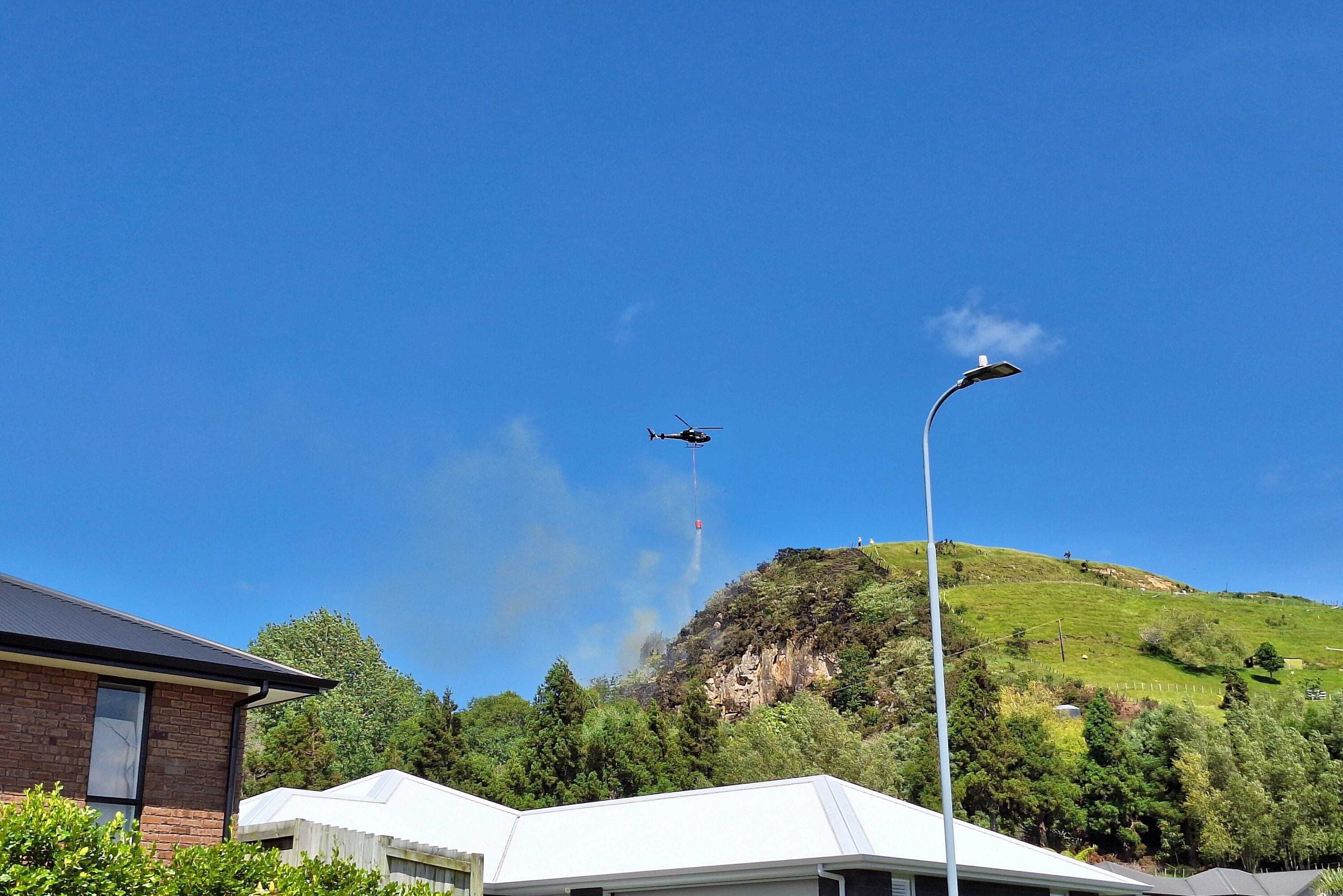 A helicopter with monsoon bucket heading toward the fire on Waikite Road.