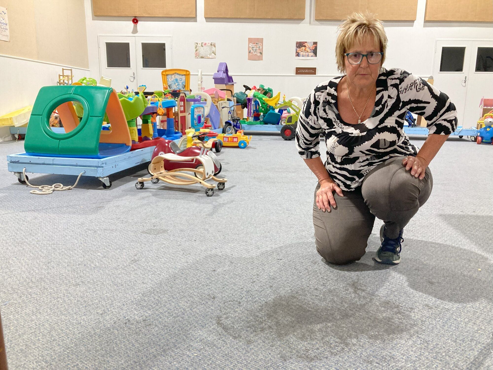  Before: Toy Librarian Sandy Goode with the worn-out, stained old carpet inside the Katikati Community Toy Library that needed replacing.